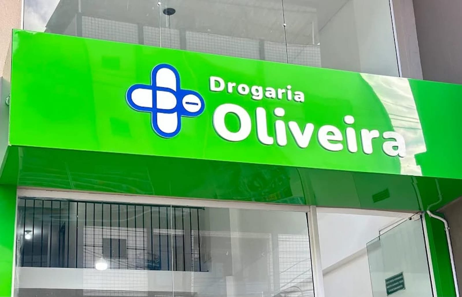 Fachada verde da Drogaria Oliveira com letreiro e cruz farmacêutica