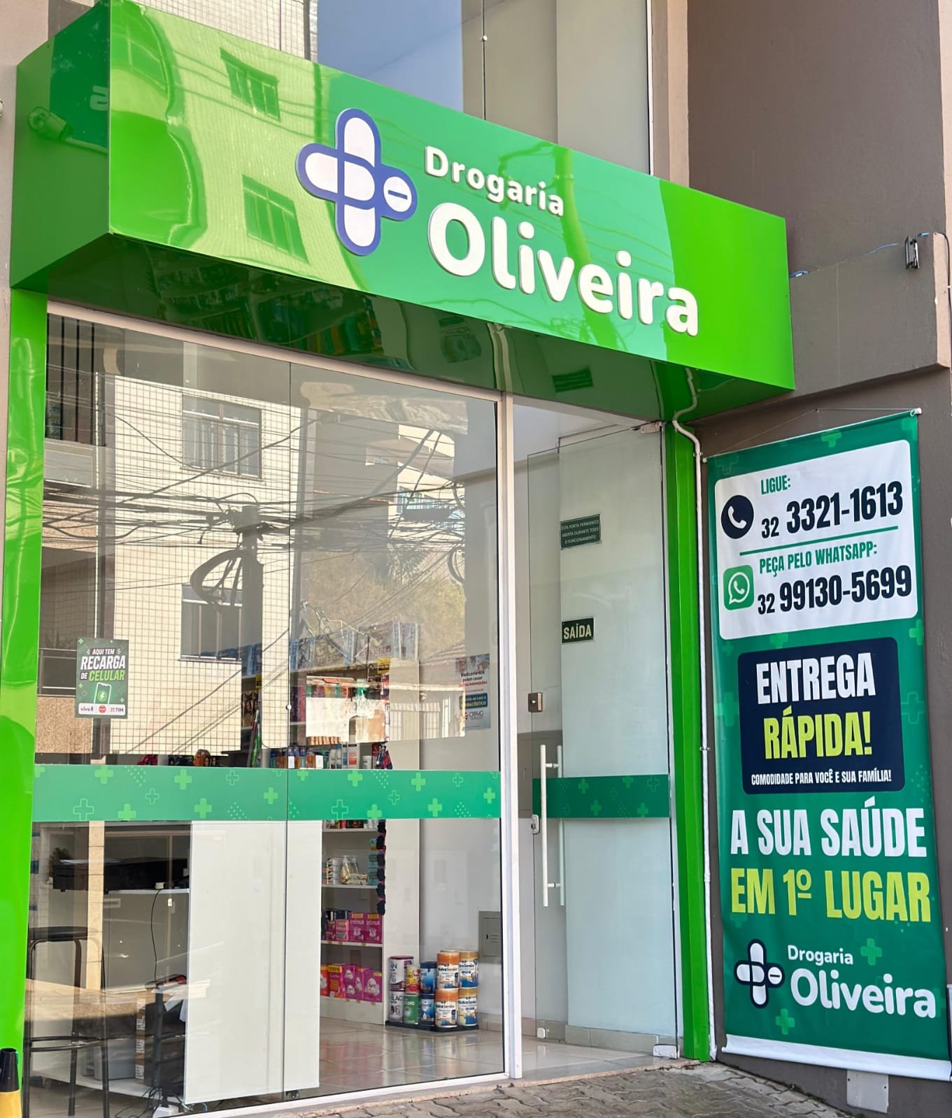Fachada da Drogaria Oliveira, com letreiro verde e cruz farmacêutica, em Juiz de Fora